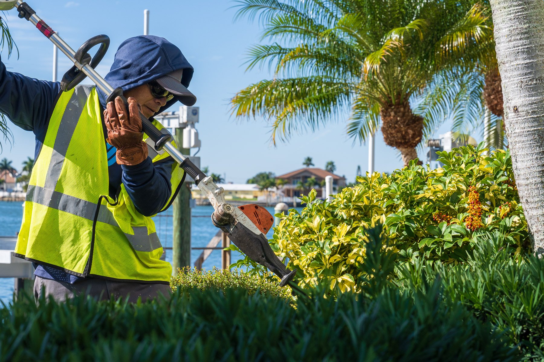 Crew member hedge trimming landscape beds near water 1