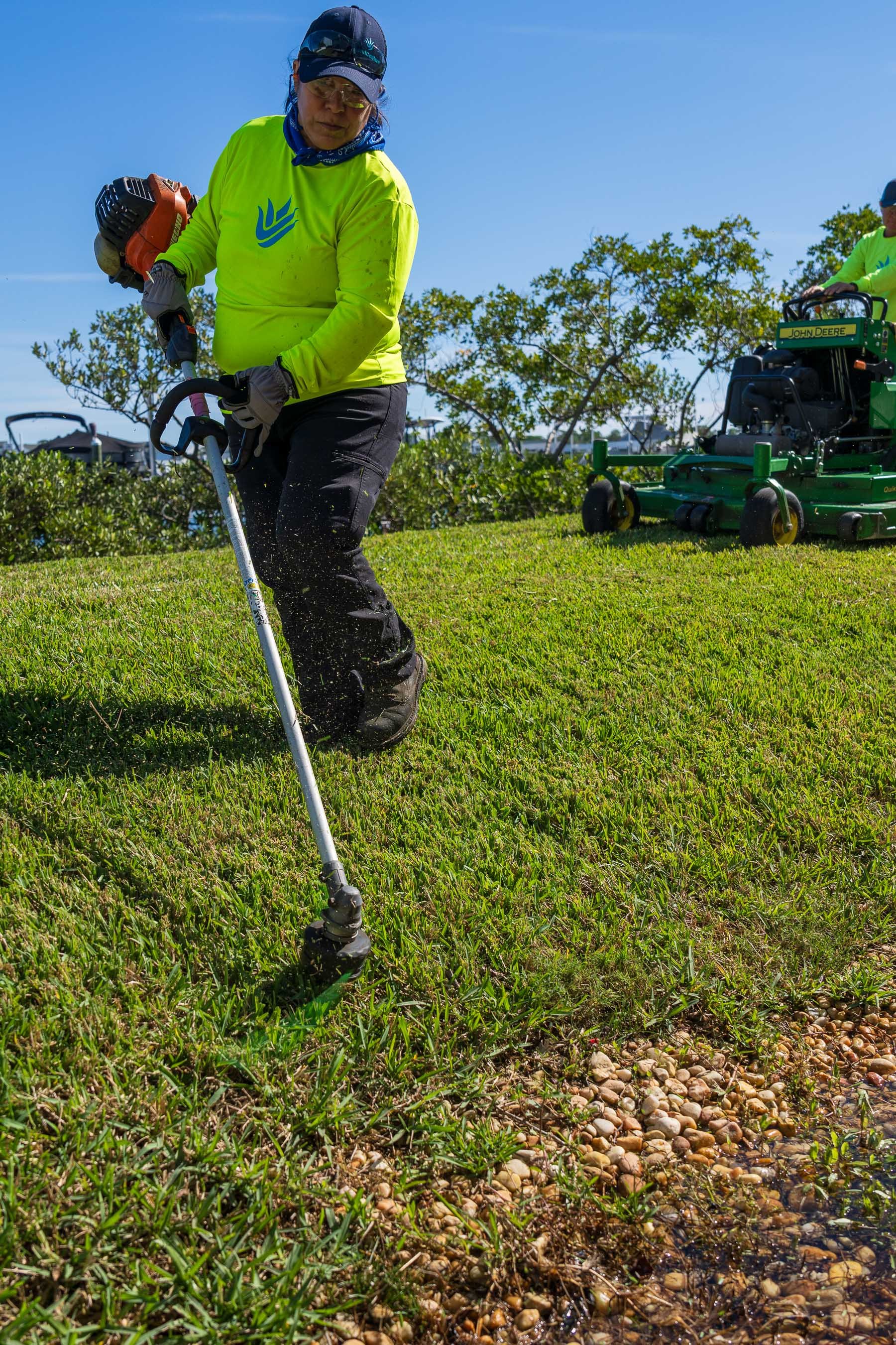 Landscape maintenance crew weed wacking along water 