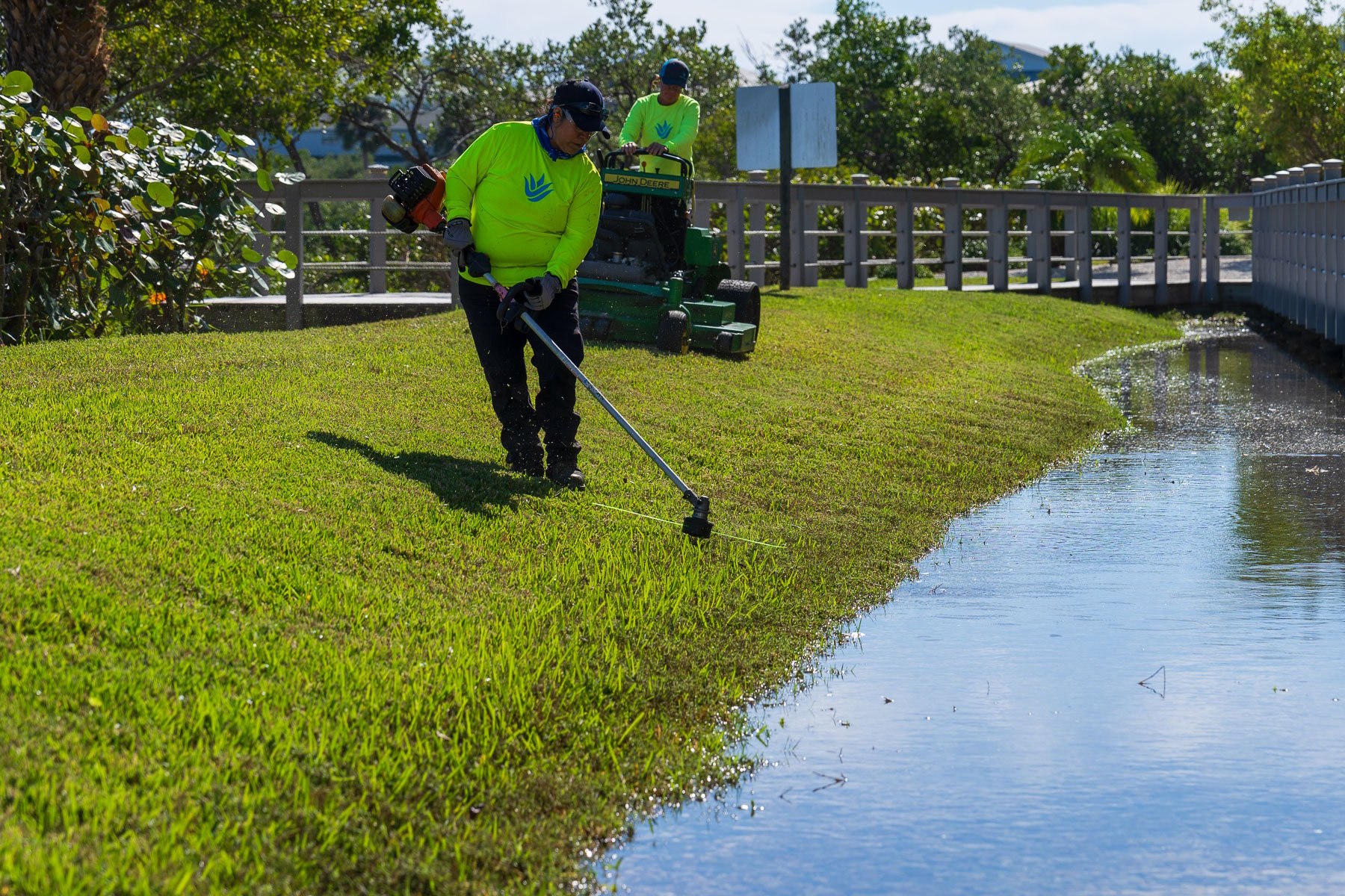 Landscape maintenance crew weed wacking along water 1