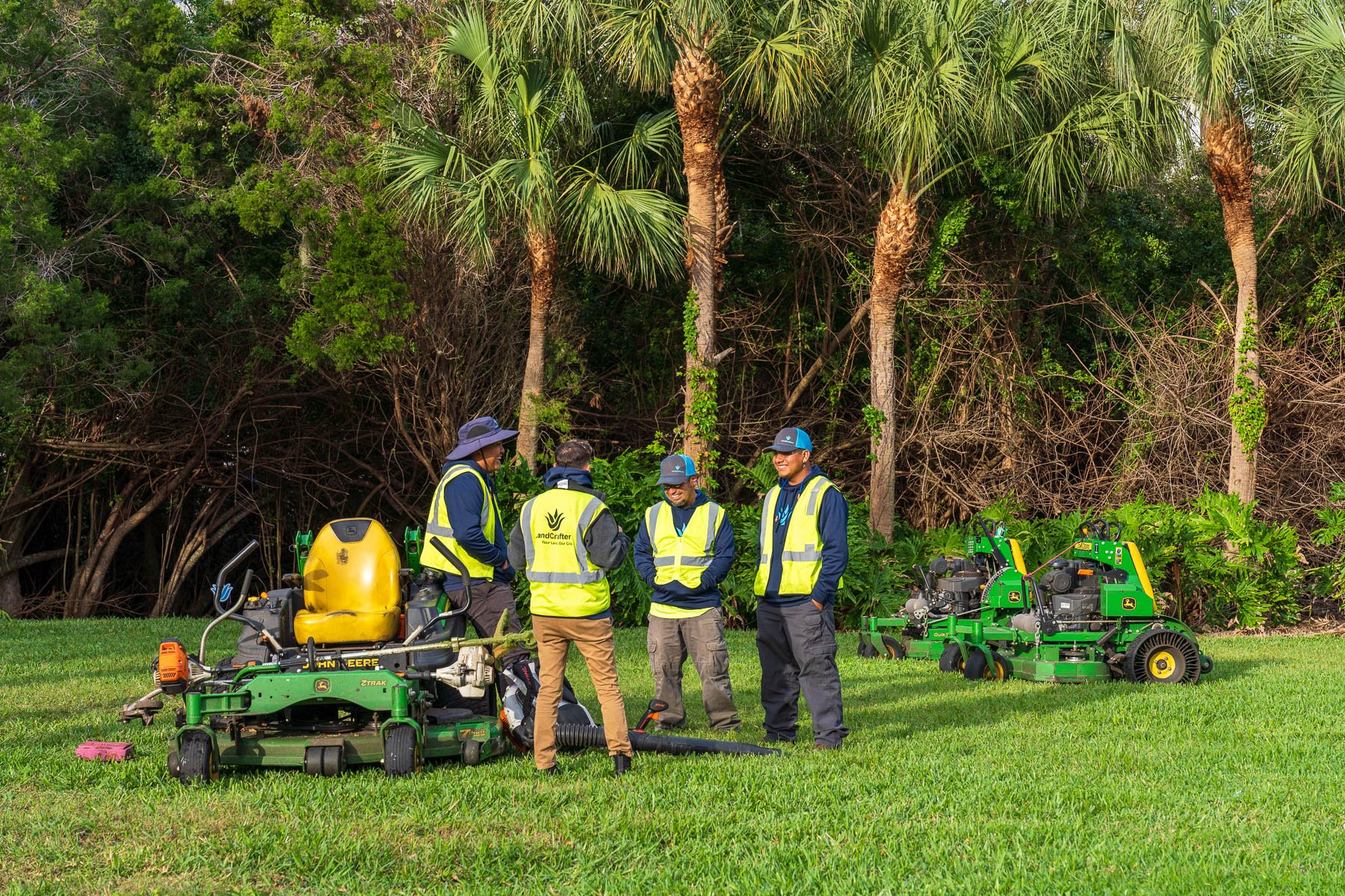 landscape crew talking near mowers with palms in background 1